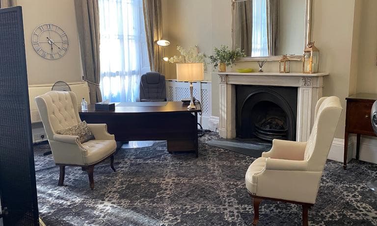A quiet consulting room at APIS Clinic: two armchairs, a desk and a period fireplace